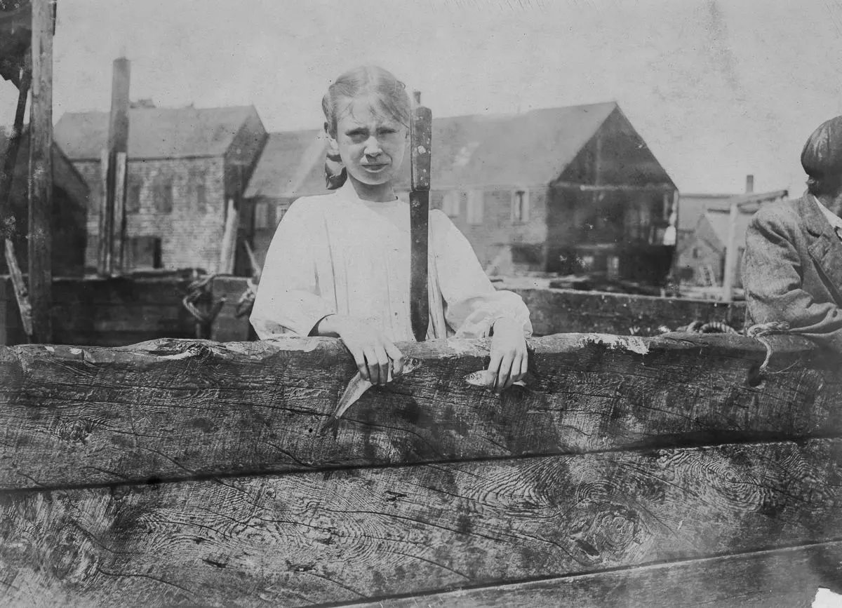 Minnie Thomas, 9 years old, showing average size of sardine knife used in cutting.