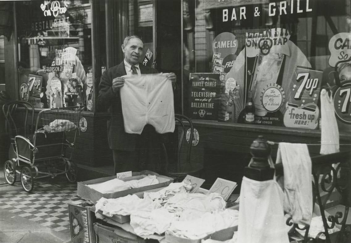 A sidewalk merchant sells clothing in front of a bar and restaurant on the Lower East Side, 1948