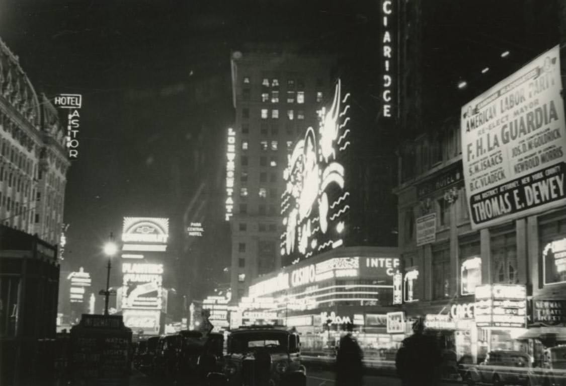 Broadway north of 42nd Street at night in Times Square with Astor Hotel to the left and an American Labor Union Party sign for Mayor F.H. La Guardia’s re-election to the right.