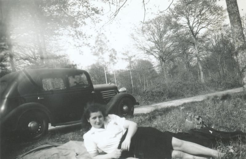 A young woman in a white blouse and a dark skirt seductively lying on a picnic blanket, 1938