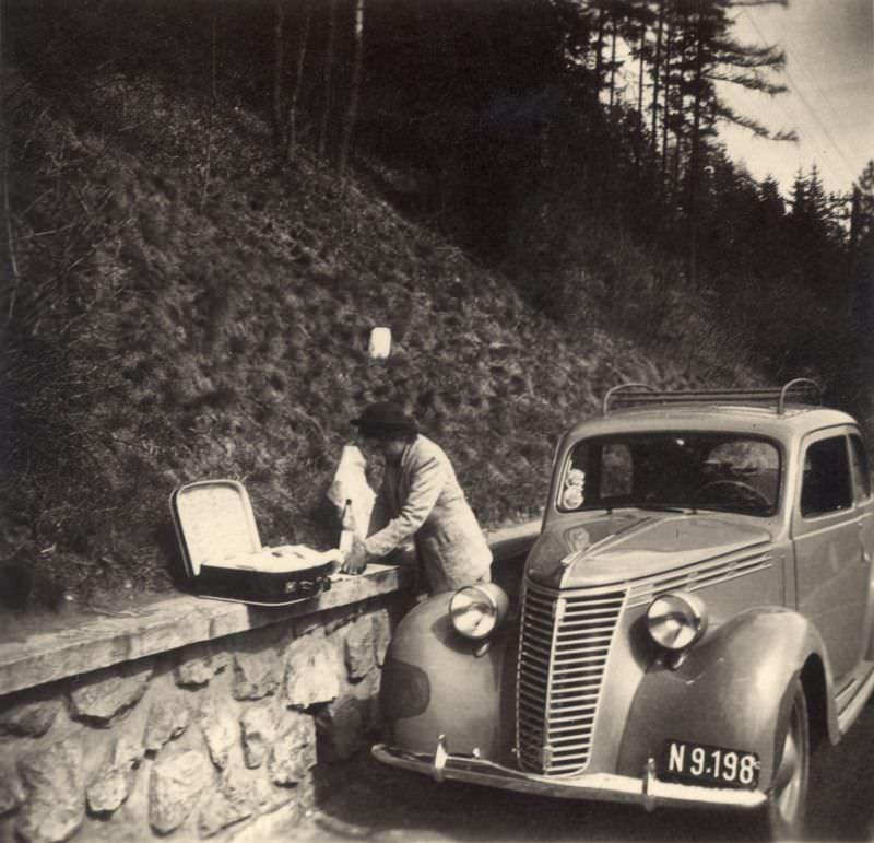 A lady preparing a roadside picnic next to a Fiat 1100 on a mountain road, 1950