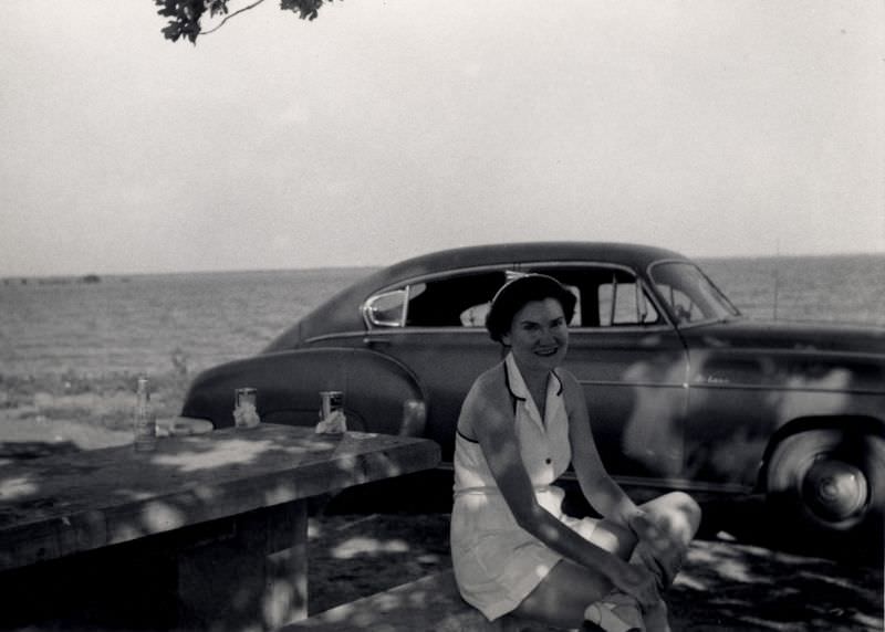 A lady in a white dress posing at a picnic table with a 1950 Chevrolet Fleetline DeLuxe, 1952
