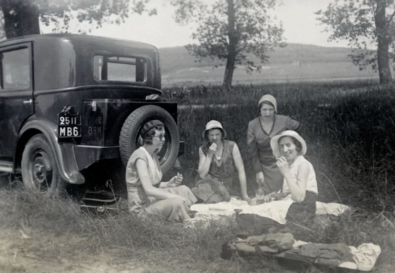 Four fashionable ladies enjoying a picnic in the countryside next to a Peugeot 201, registered in the French département of Nord, 1932