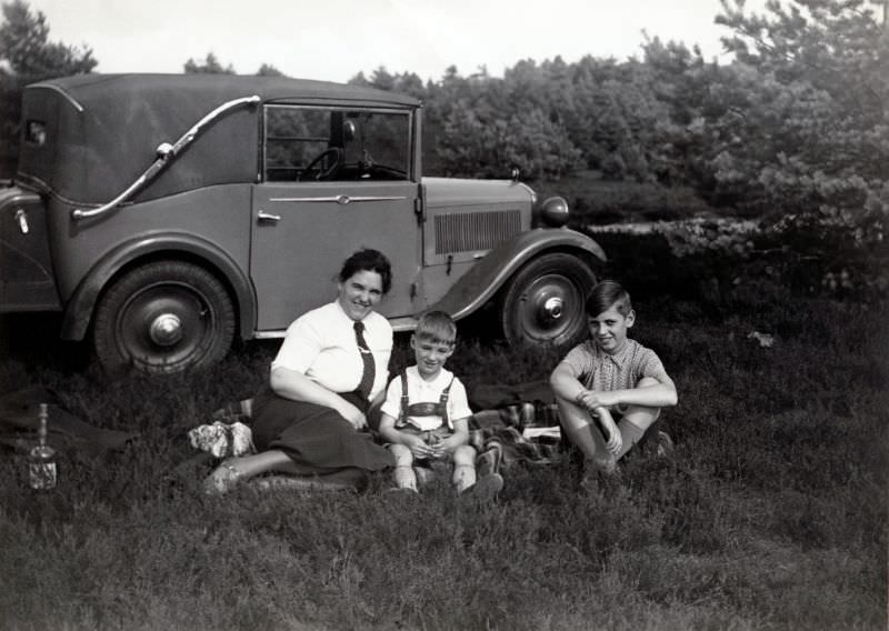 A lady dressed in a white blouse and tie and her two sons enjoying a picnic in the countryside, 1935