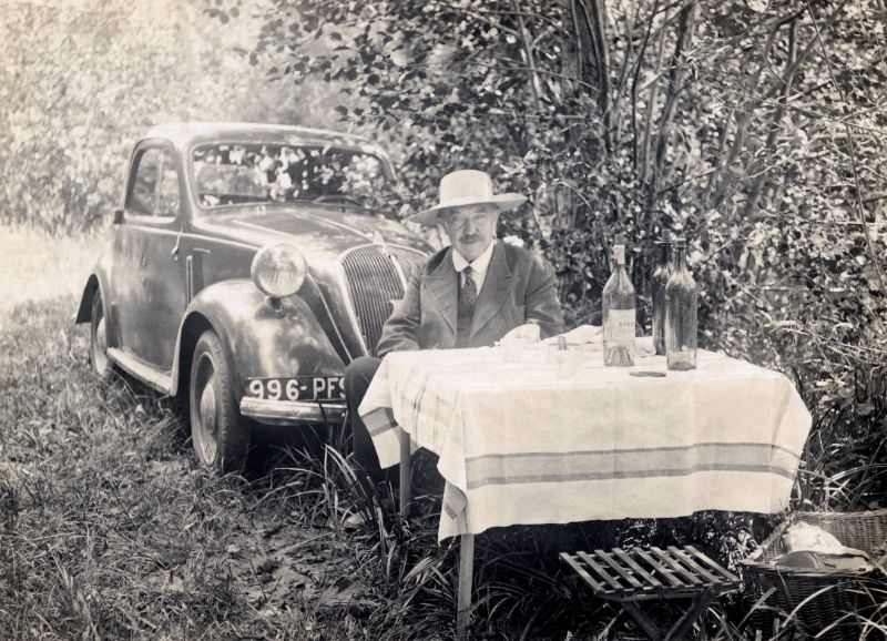 A middle-aged fellow in a suit and tie posing at a picnic table in the countryside, 1938