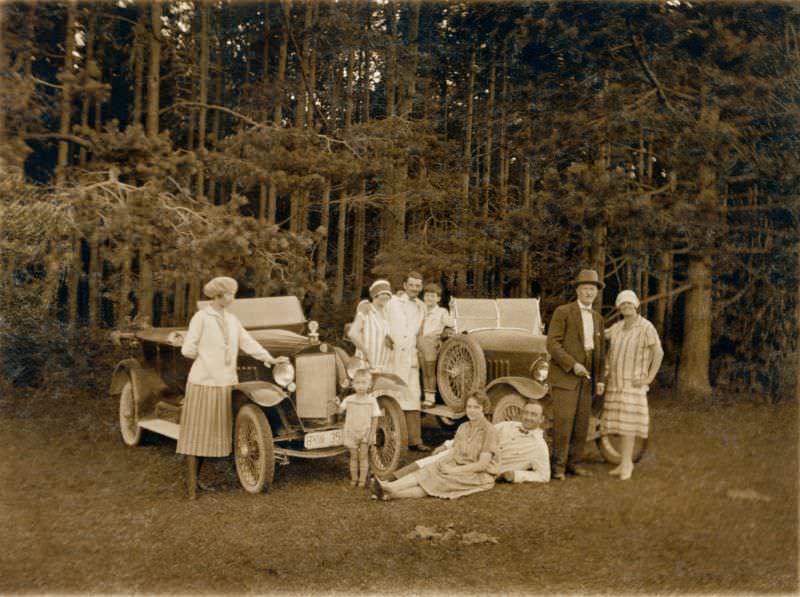 A company of nine posing with two early Steyr Typ IV open tourers in the countryside, 1925