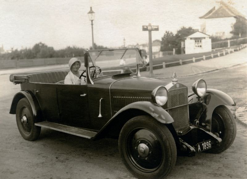 A fashionable lady dressed in white posing in the driver's seat of a Steyr XII Double Phaeton convertible in a suburban streetm, 1930