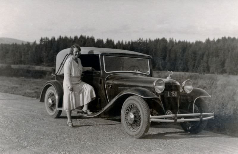A fashionable lady in a white dress posing with a Steyr 30 Sport-Cabriolet on a gravel road in the countryside, 1932