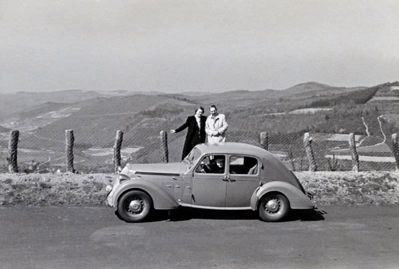 A couple posing with a Steyr 220 Limousine on a mountain road overlooking a valley, 1938