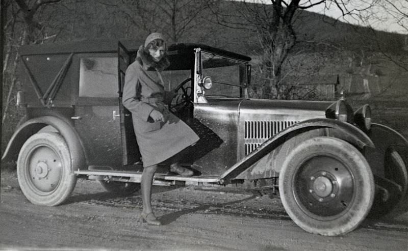 A stylish lady posing with a mud-splattered Steyr XII on a dirt road in wintertime, 1927