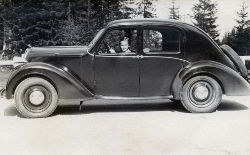A young girl posing in the driver's seat of a Steyr 100 on a country road in midday sunshine, 1938