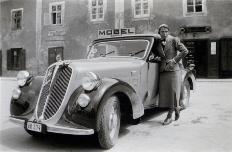 An elegant lady in a female suit posing with a Steyr 120 Super in a village street, 1938