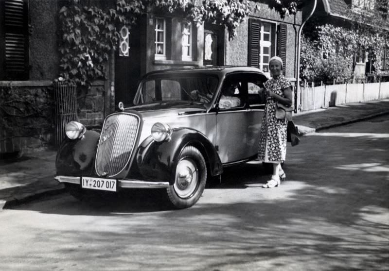 An elegant lady in a floral summer dress posing with a Steyr 200 in a residential street. The car is registered in the administrative region of Düsseldorf, 1938