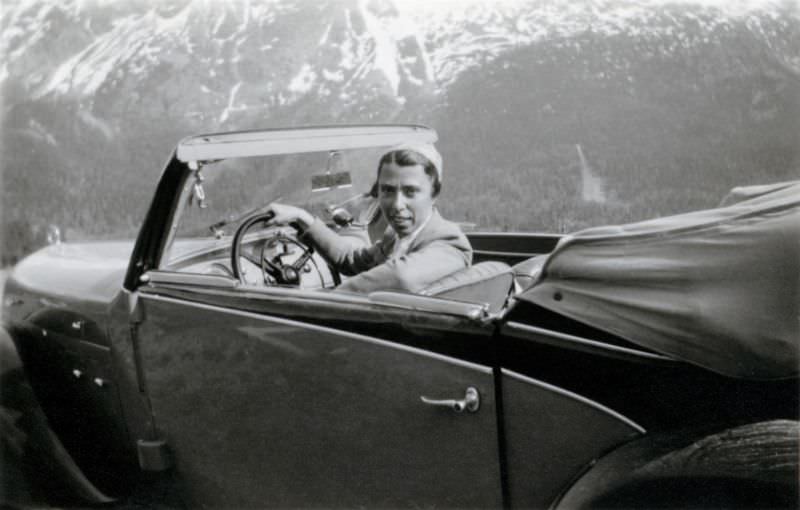 An elegant lady posing in the driver's seat of a two-tone Steyr 120 Super in an Alpine setting, 1938