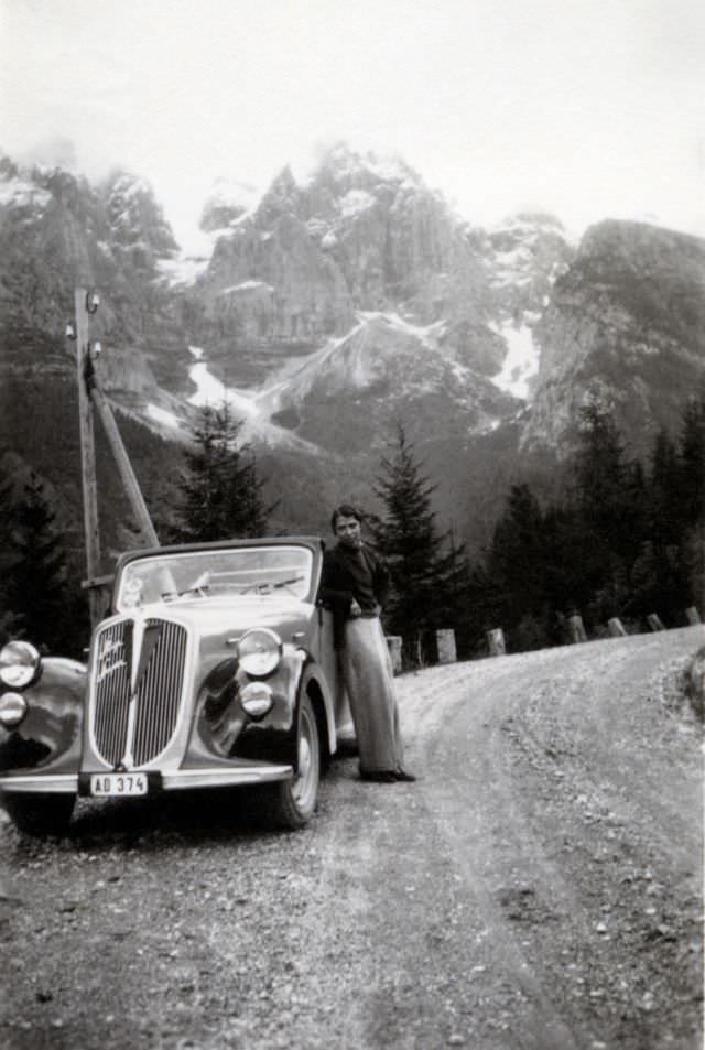 An elegant lady posing with a Steyr 120 Super on a graveled mountain road in an Alpine setting, 1938