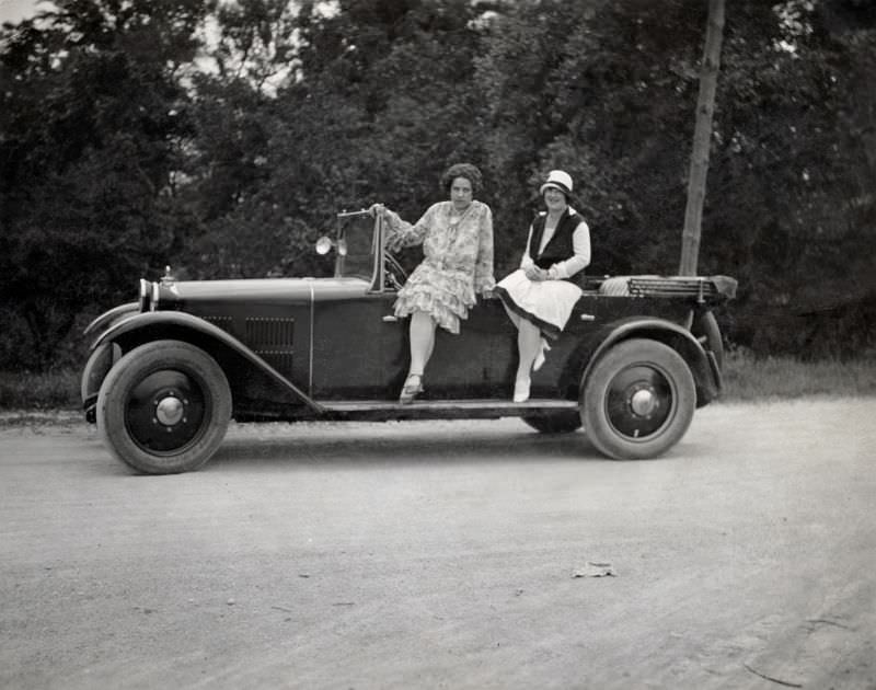 Two fashionable ladies – possibly sisters – posing with a Steyr XII convertible on a gravel road in summertime, 1928