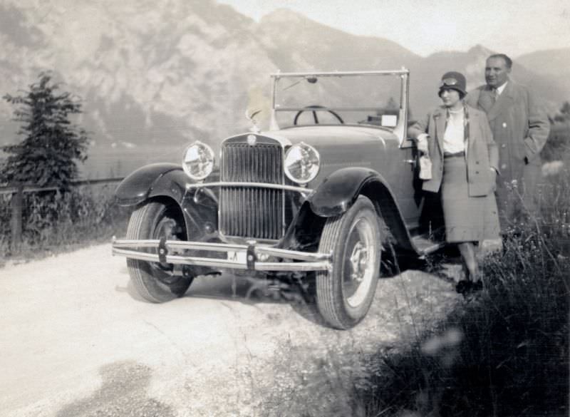 A well-to-do couple posing with a Steyr XX Double Phaeton on a gravel road by the side of a lake in summertime, 1929
