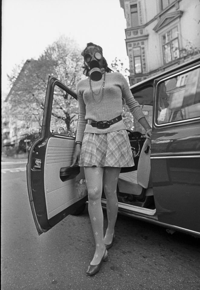 Air pollution, young woman wearing a gas mask stepping out of her car, 1970