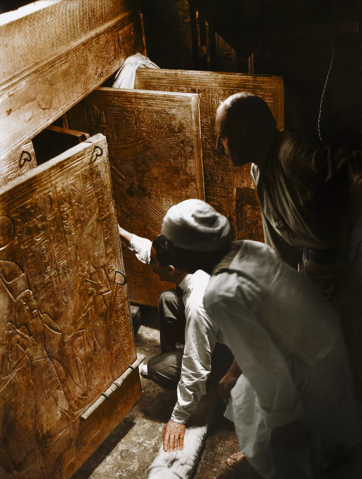 Howard Carter (kneeling), Arthur Callender and an Egyptian workman in the Burial Chamber, looking through the open doors of the four gilded shrines towards the quartzite sarcophagus. Tutankhamun's Tomb, October 1926