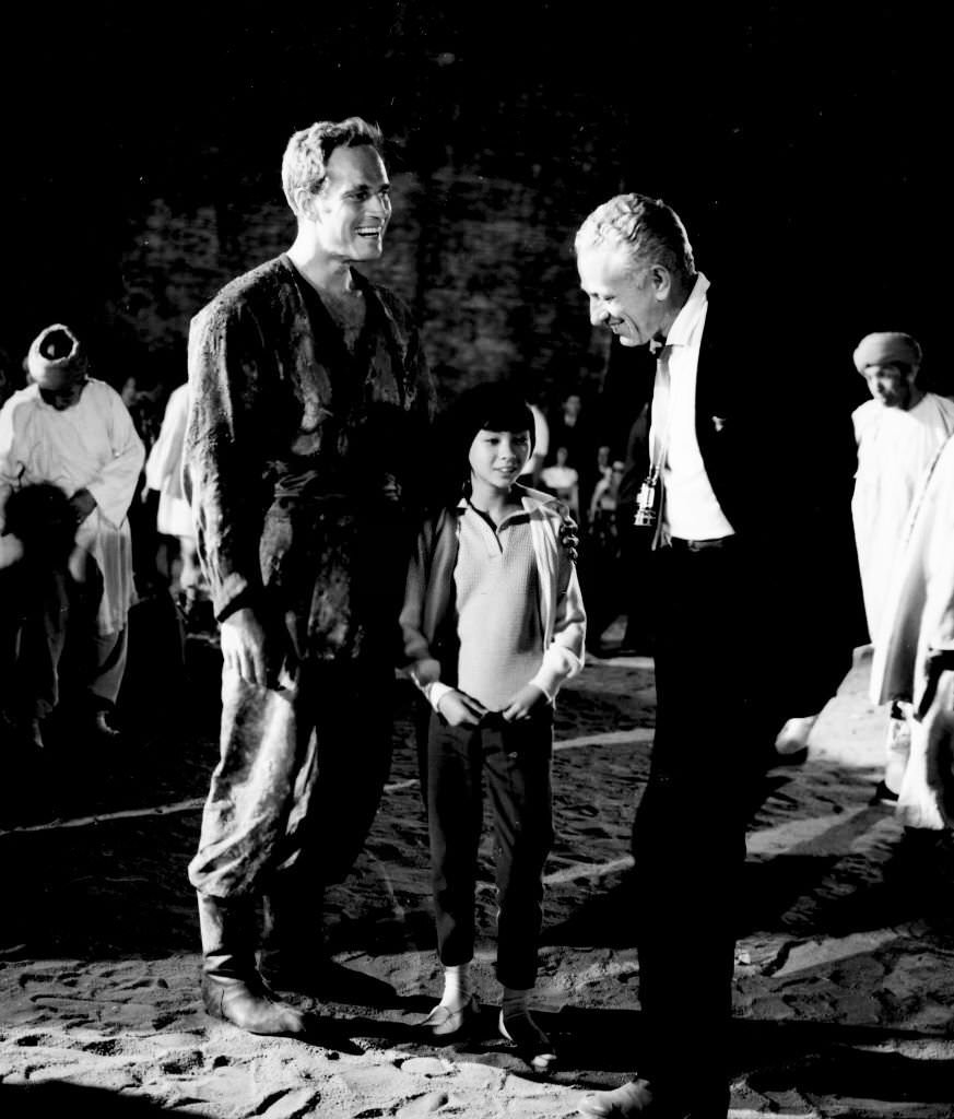 Charlton Heston and Lynne Sue Moon chat with director Nicholas ray on location in Madrid for the movie '55 days of Peking', 1963