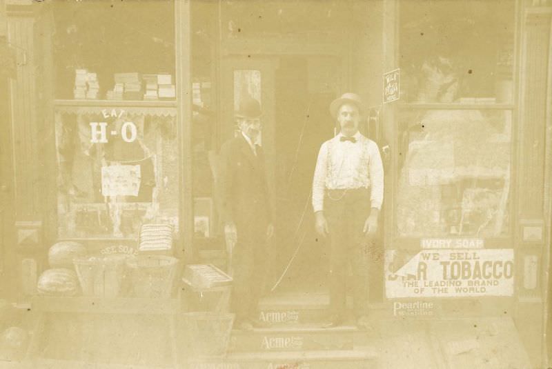 Two men outside grocery store, 1880s