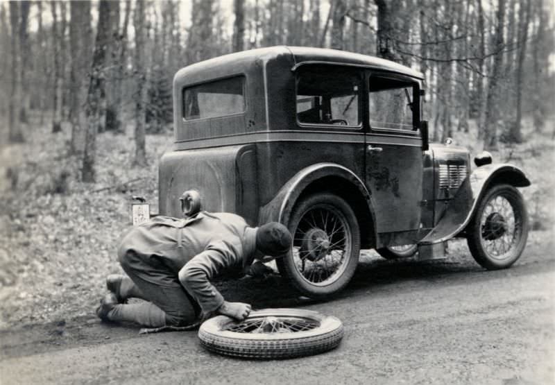 A fellow experiencing tyre trouble with a BMW 3/15 PS on a gravel road in a forest in wintertime, 1930