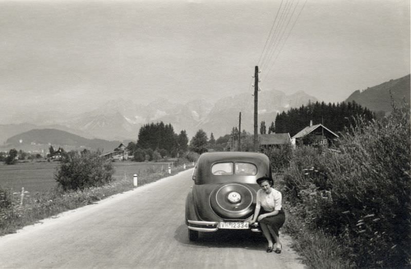 A young lady posing on the bumper of a BMW 326 on a country road, 1938.