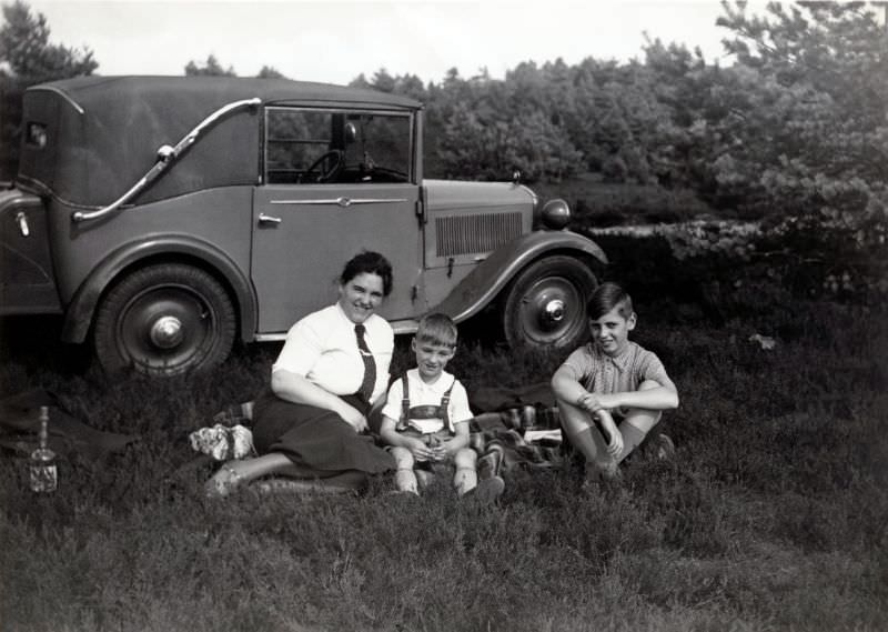 A lady dressed in a white blouse and tie and her two sons enjoying a picnic in the countryside, 1935