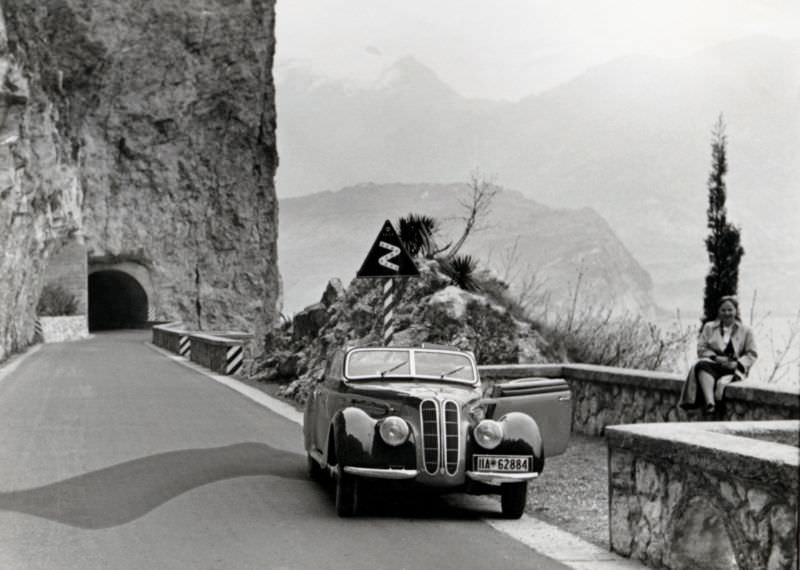 A lady posing with a BMW 327/28 Cabriolet convertible by the side of the coastal road at Lake Garda, 1939.
