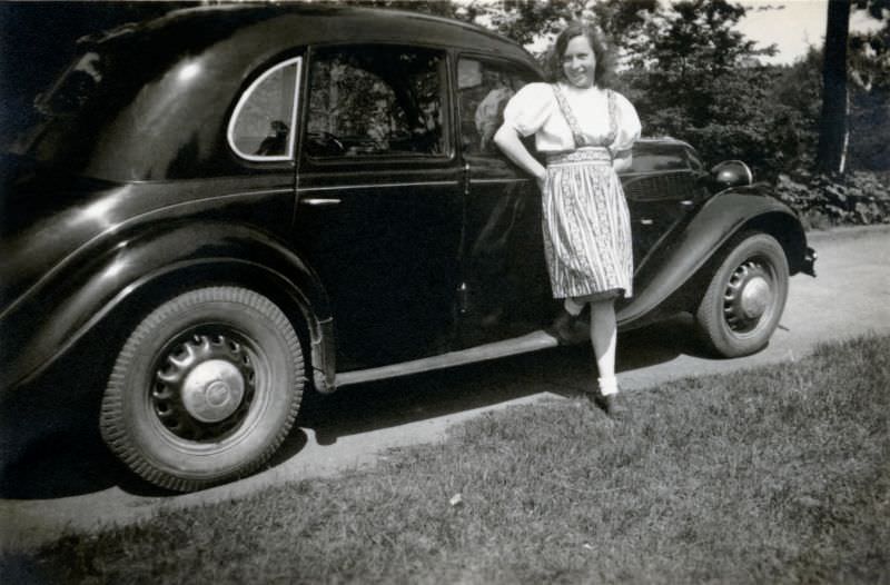 A young lady in a fashionable Dirndl-style dress posing with a BMW 326 in the countryside, 1948