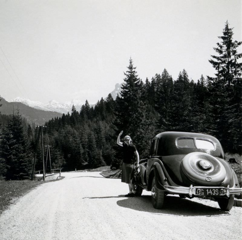 A blonde lady posing next to a pre-war BMW 326 on an Alpine road, 1950.