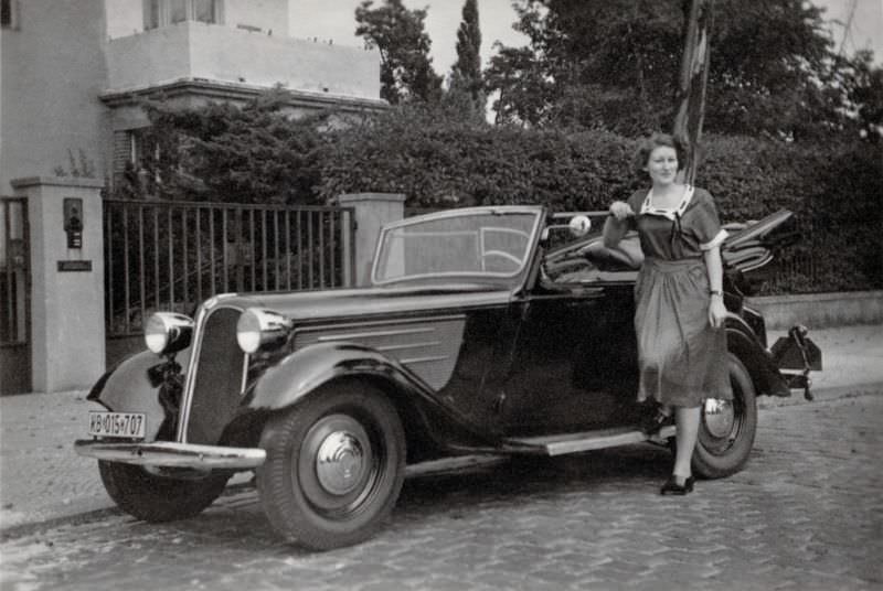 An elegant lady posing with a BMW 319 Cabriolet convertible in a cobbled street in an upper-middle-class neighborhood, 1950.