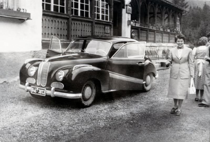 A cheerful lady in a female suit posing with a BMW 501 in the drive of a hotel, probably somewhere in the Black Forest, 1955.