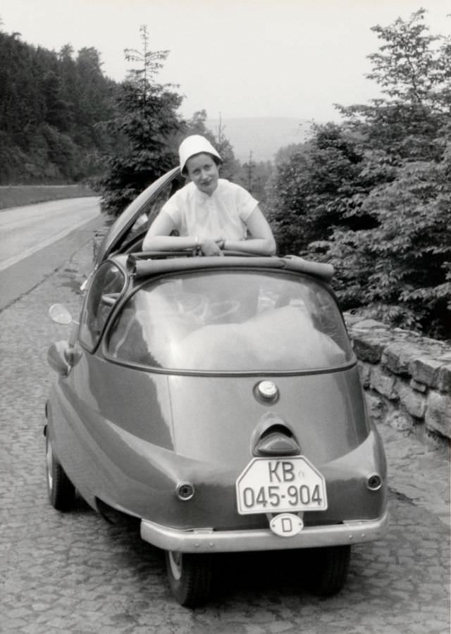 A lady wearing a white blouse and hat posing with a BMW Isetta on a mountain road, 1956.
