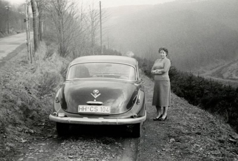 A lady wearing a 3/4-length skirt posing with an eight-cylinder BMW 502 on a mountain road, 1958.