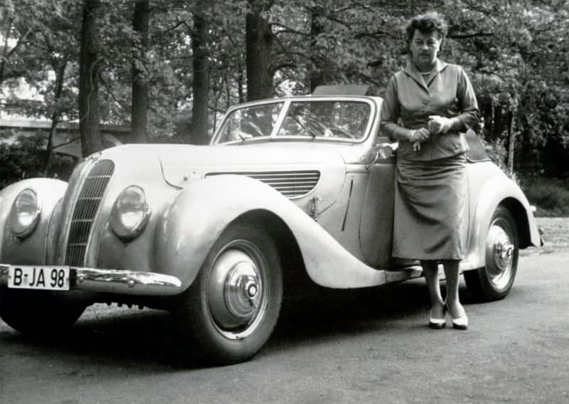A middle-aged lady in a female suit posing with a slightly shabby BMW 327/28 in summertime, 1958.