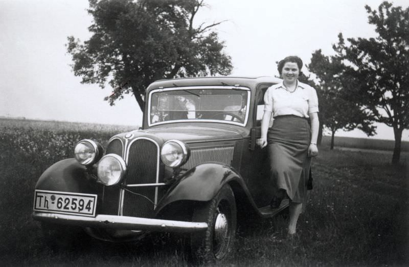 A young lady wearing a white blouse and a dark skirt posing with a BMW 315 in the countryside, 1935.