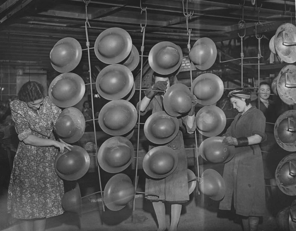 Women workers hang out tin hats which have just been spray painted, to dry, 1940.