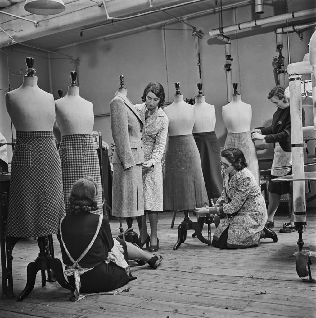 Four seamstresses make final adjustments to utility suits and skirts at a Bourne and Hollingsworth department store workroom in London during World War II.