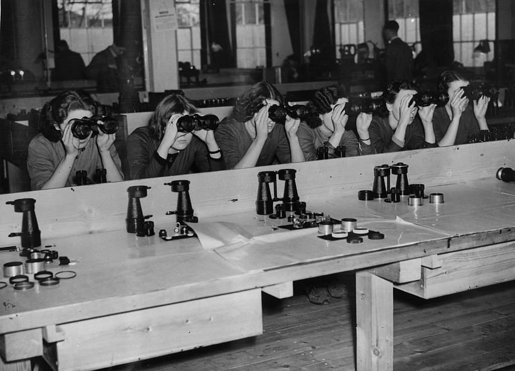 Workers in one of the largest optical instrument making factories in Britain, where binoculars, telescopes, photographic lenses and other scientific devices are made for the armed forces.
