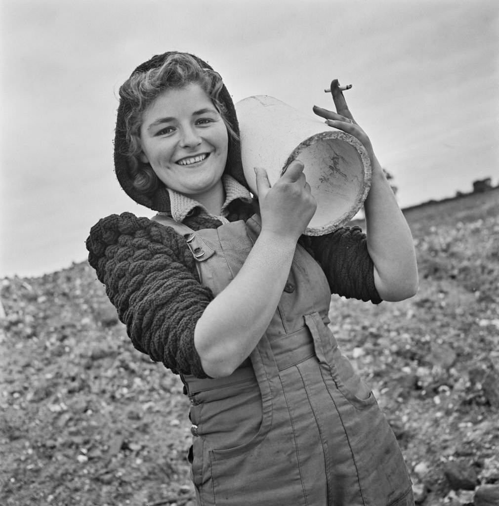 Mrs Peggy Devine, an evacuee from London, holds a section of pipe as she carries out rough navvying work on the site of a new aerodrome being constructed in East Anglia during World War II on 16th September 1941.
