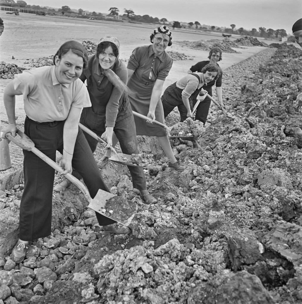 Holding shovels, a group of female construction workers fill in drainage trenches as they carry out rough navvying work on the site of a new aerodrome being built in East Anglia during World War II on 16th September 1941.