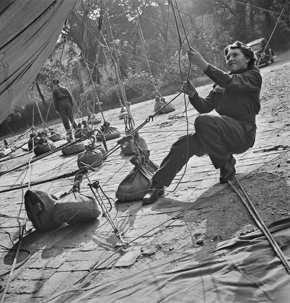 A member of the Women's Royal Air Force (WRAF) pulls on a rope to tighten up lines to a barrage balloon tethered in Grosvenor Gardens, London, September 1941.