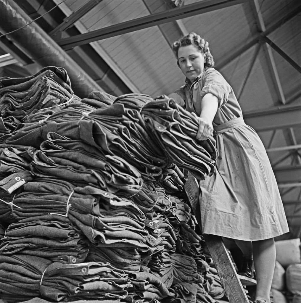 Female warehouse worker Dorothy Durber handles bundles of khaki standard issue military uniform at a Central Ordnance Depot for British Army uniform and equipment in England, 1941.