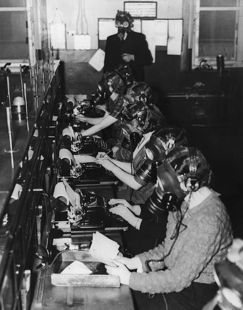Teleprinter telephone operators at work during a 15-minute gasmask drill, Scotland, 24th April 1941.