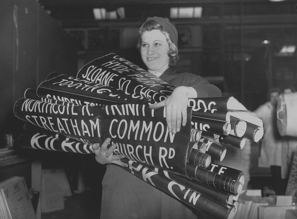 Woman war worker E Oakham, carrying bus destination signs at the London Passenger Transport Board, 1941