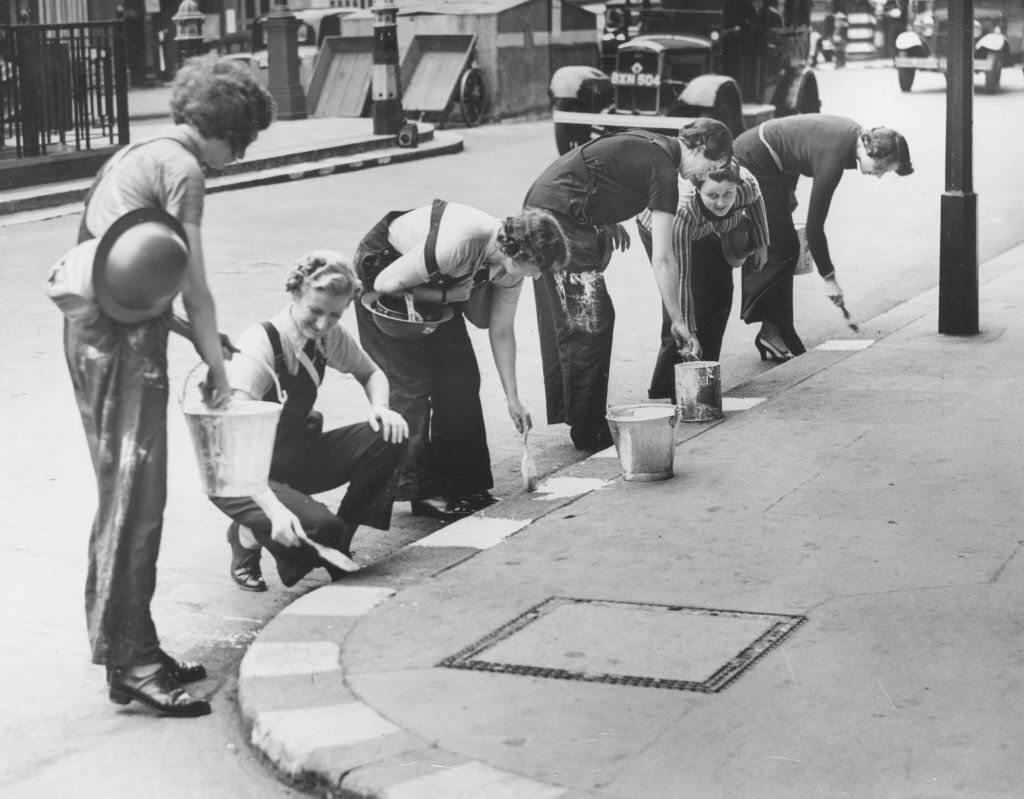 Women in a civil defence unit paint white squares along the kerb to facilitate night-time driving in London, 1939