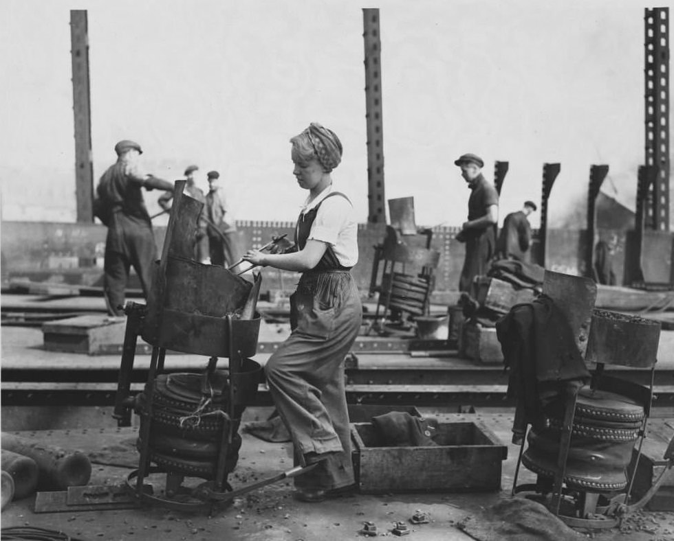 A woman heating a rivet on a ship under construction. Women have entered previously male job fields in England during wartime, specifically shipbuilding.
