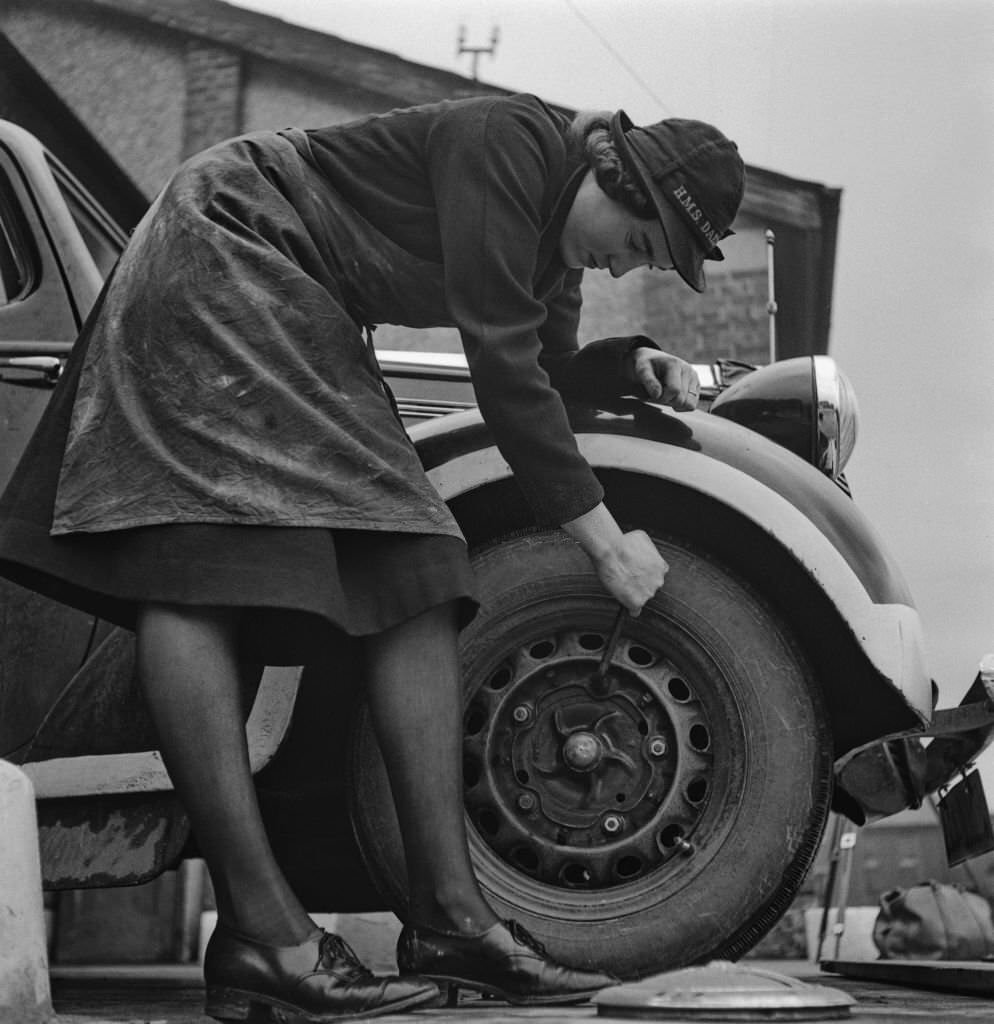 A member of the WRNS (Women's Royal Naval Service), the women's branch of the Royal Navy, changing the tyre of a car during her tour of duty on the 'HMS Daedalus' during World War II, UK, March 1941.