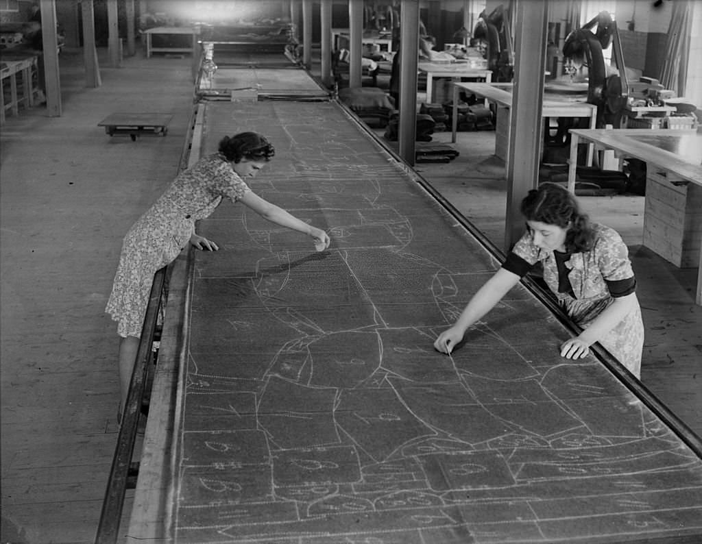 Women marking the pattern of uniforms onto material with chalk in preparation for the cutting stage of the process. Nine hundred miles of khaki serge produces 5,000,000 battle suits and 6,000,000 pairs of trousers.
